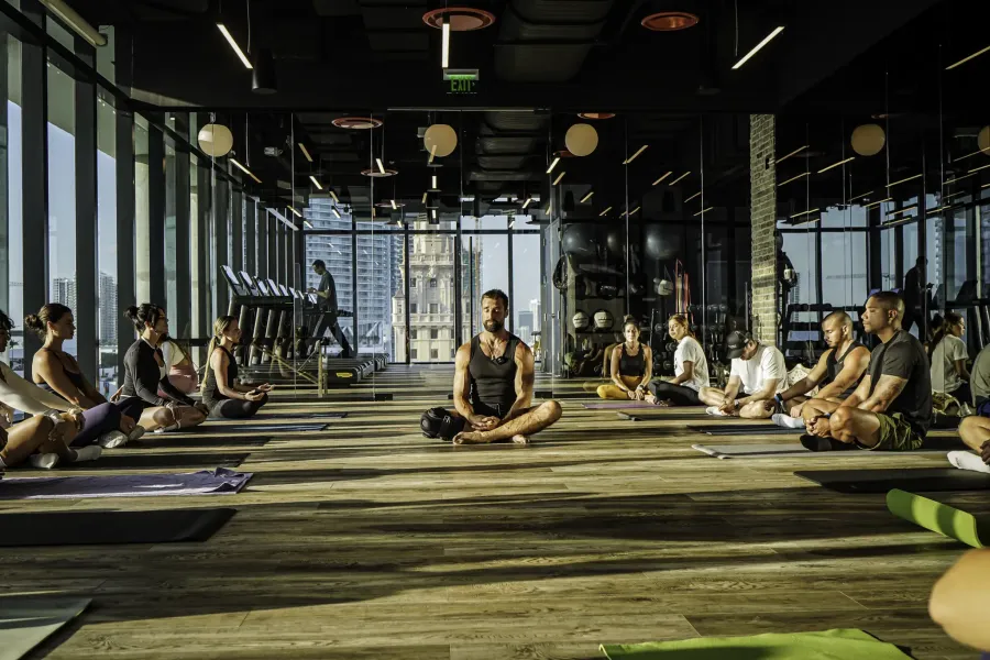 Indoor sunset yoga session at Biohack Miami inside The Elser Hotel, with attendees practicing mindfulness and wellness in a panoramic glass-walled studio overlooking downtown Miami